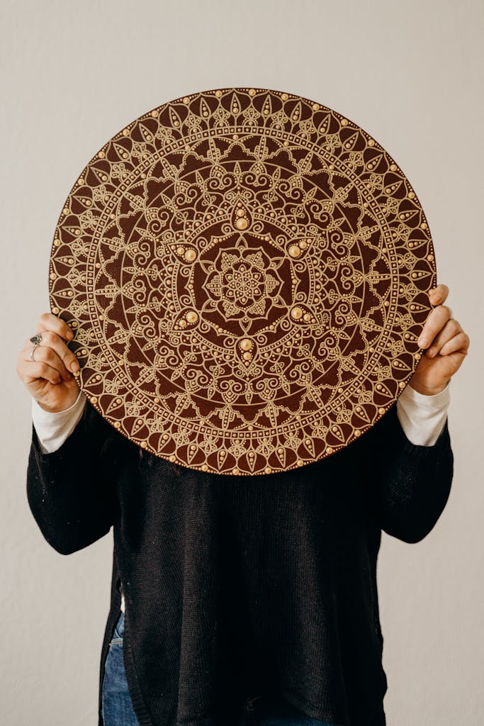 A person holding a detailed round mandala with a beige background, perfect for decor inspiration.