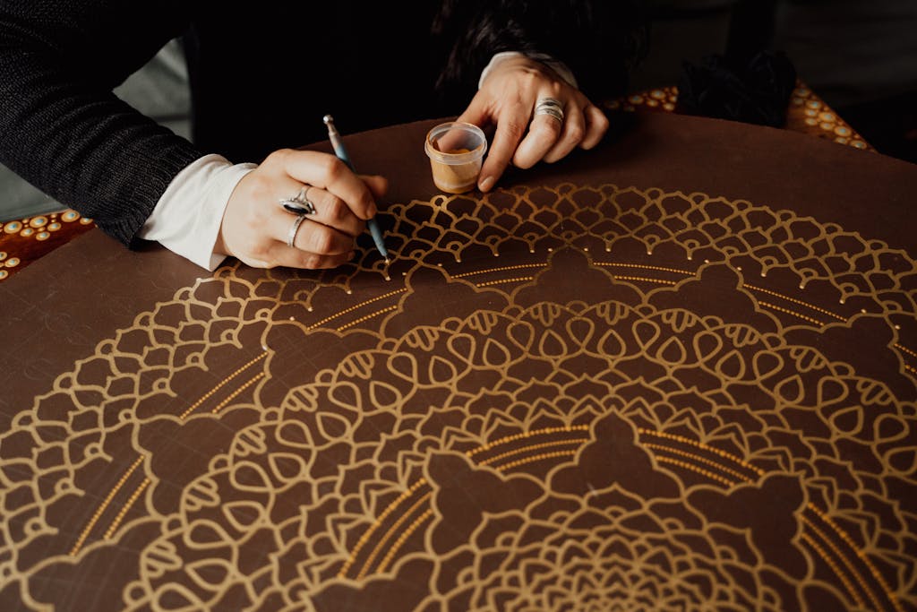 Close-up of hands crafting a golden mandala pattern on a table.